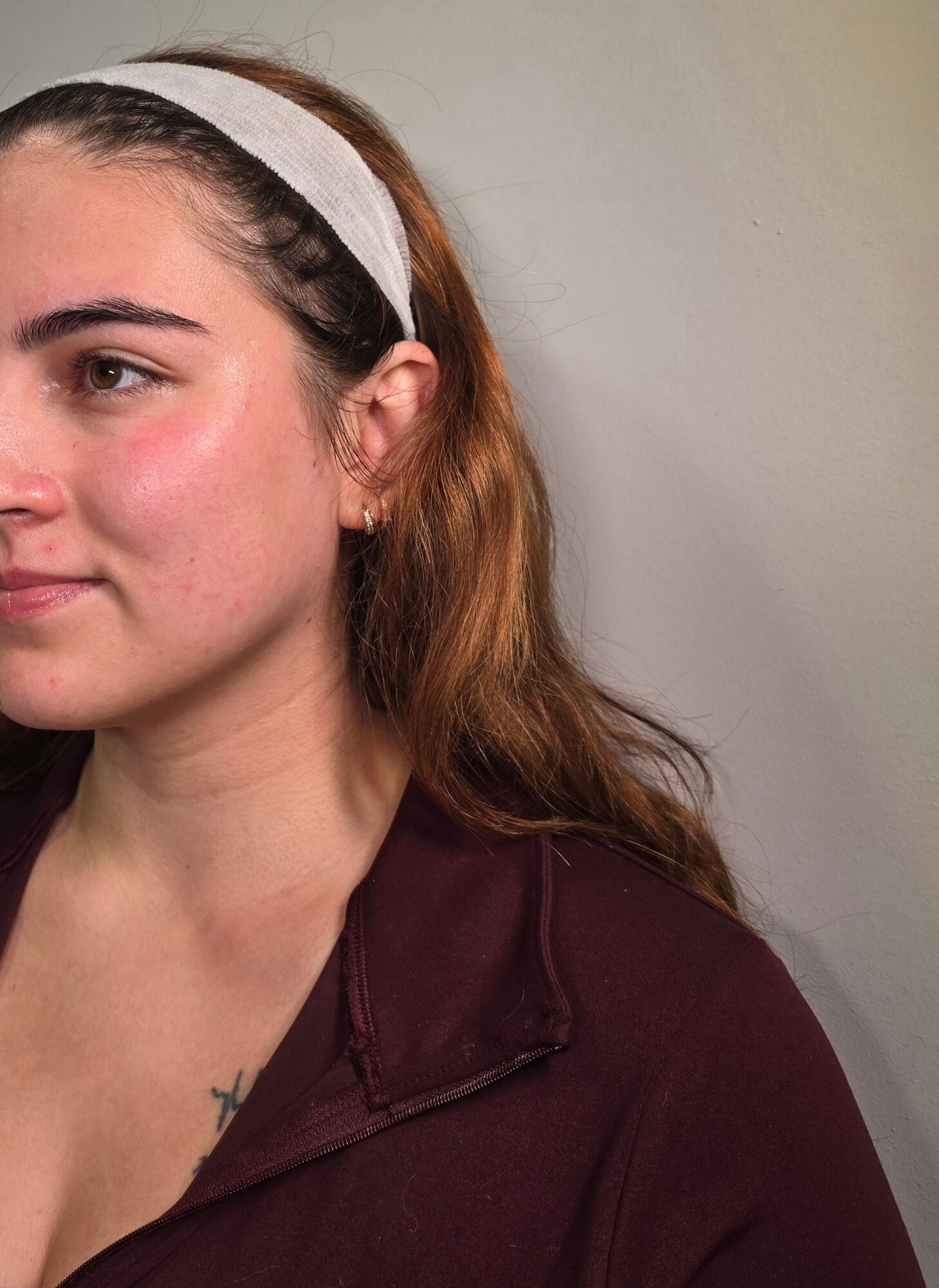 Close-up portrait of a person with a white headband and burgundy top against a plain wall.