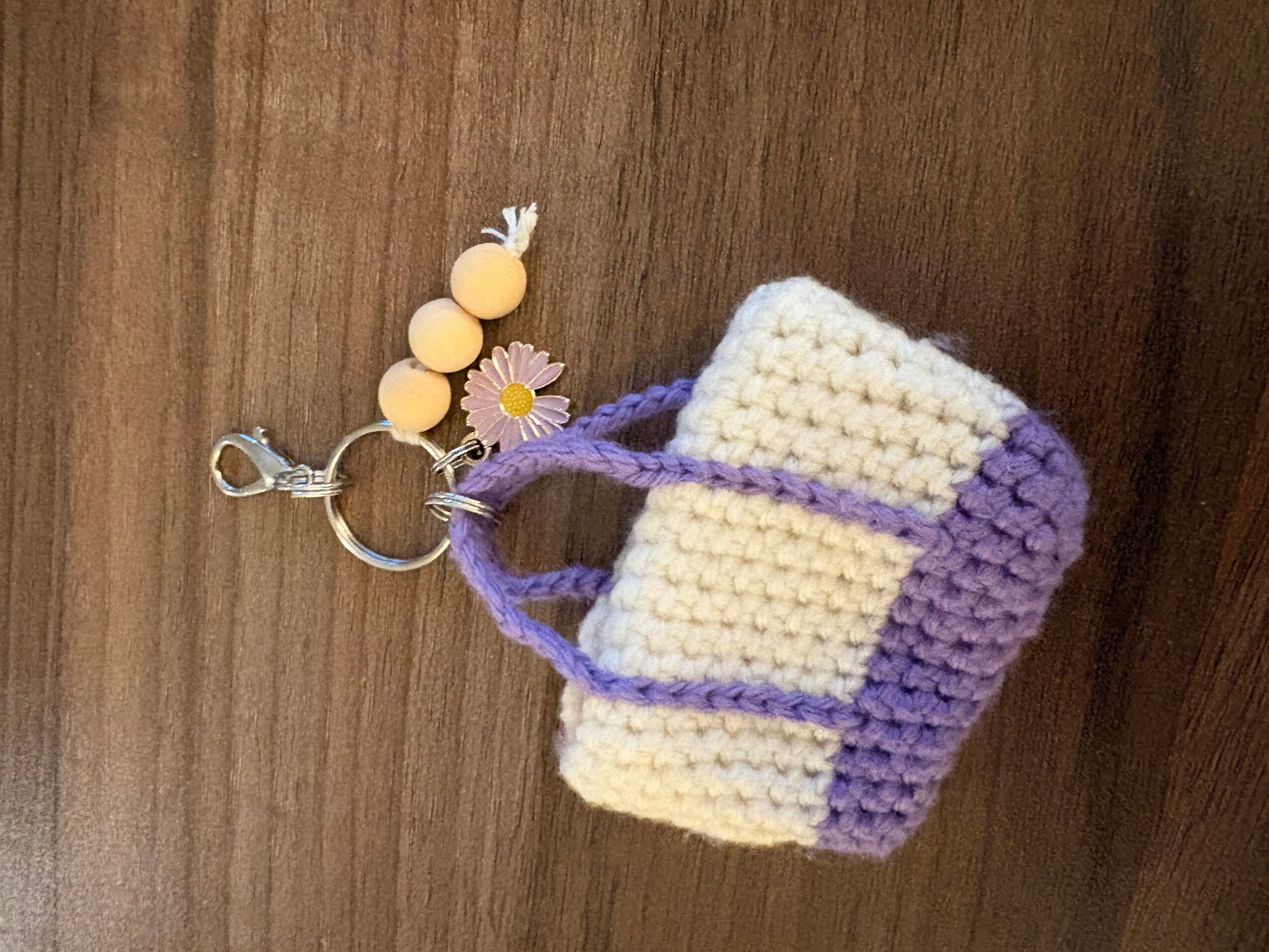 Small crocheted cream-and-purple pouch attached to a metal keyring with yellow beads and a flower charm.