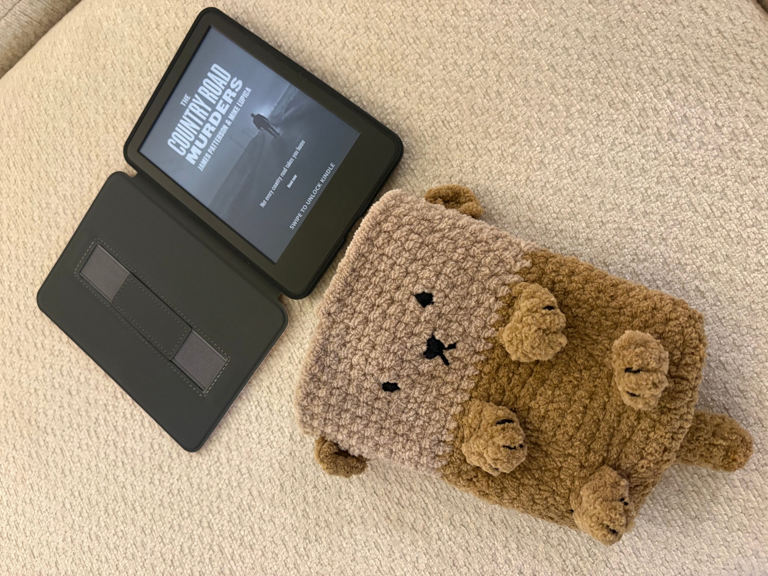 An e-reader and crocheted brown animal-shaped pouch rest on a beige carpet.